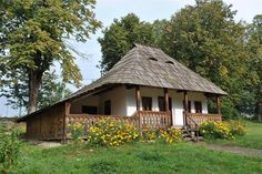 a small house with a thatched roof and flowers in the foreground, surrounded by trees