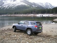 a jeep parked on the side of a lake with mountains in the backgroud