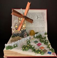 an open book with a paper model of a house and windmill on top of it