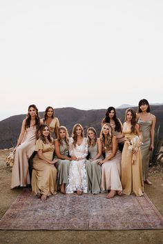 a group of bridesmaids sitting on top of a rug in the middle of a desert