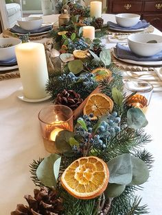 the table is set with pine cones, oranges and candles