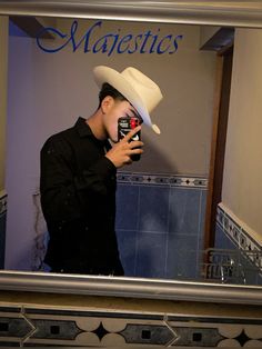 a man taking a selfie in front of a mirror wearing a white cowboy hat