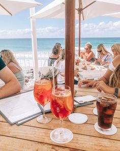 people sitting at an outdoor table with drinks and menus on it, overlooking the ocean