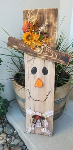 a wooden sign with a scarecrow wearing a hat on it's head next to a potted plant