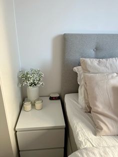 a bed with white sheets and pillows next to a night stand with two candles on it