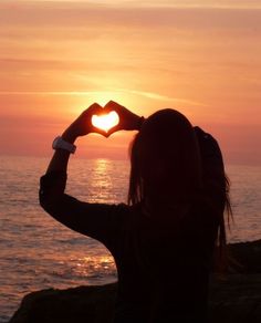 a woman making a heart shape with her hands on the beach at sunset or sunrise