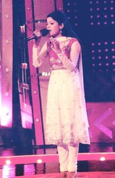 a woman standing on top of a stage holding a microphone in her hand and singing