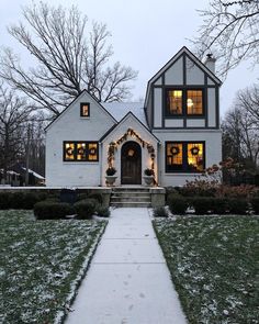 a white house with snow on the ground and trees in the front yard at night