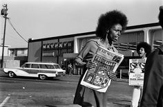 an old black and white photo of a woman holding a news paper in the street