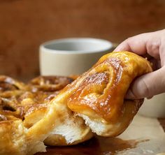 a person holding a pastry in front of a plate with some food on it and a cup