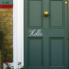 a green door with the word hello written on it and flowers in front of it