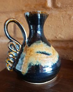 a black and gold vase sitting on top of a wooden table next to a brick wall