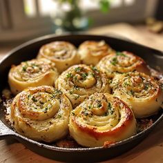 a skillet filled with cinnamon rolls on top of a wooden table