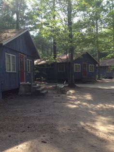 there is a blue cabin in the woods with trees around it and two chairs on the ground