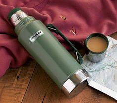 a map, cup of coffee and a thermos sitting on a table next to a red shirt