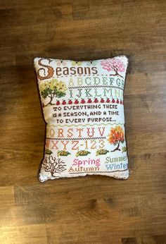 a cross stitch pillow sitting on top of a wooden floor with the words season's greeting