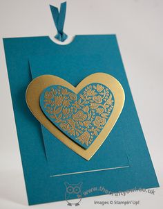 a blue and gold heart shaped card on a white surface with a string attached to it