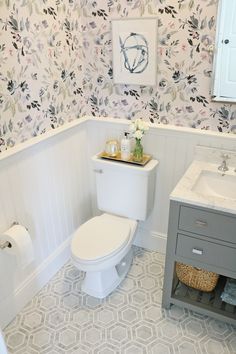 a white toilet sitting next to a sink in a bathroom under a painting on the wall