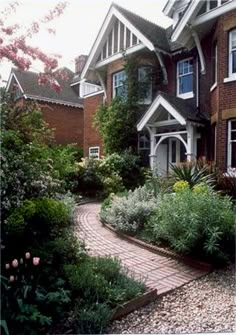 a brick pathway leading to a house with lots of flowers and trees in the front yard