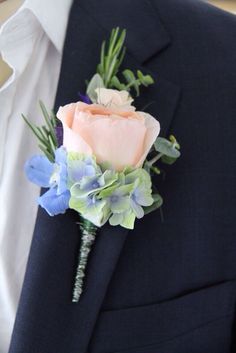 a boutonniere with blue flowers and greenery on the lapel of a man in a suit