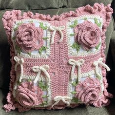 a pink crocheted pillow with roses on the front and sides, sitting on a couch