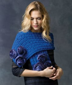 a woman wearing a blue crocheted ponchy with roses on it and holding her hands in her pockets