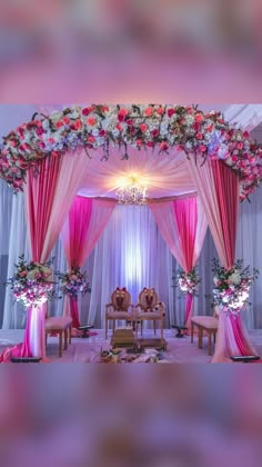 a wedding stage decorated with pink drapes and floral arrangements on the ceiling, along with two wooden chairs