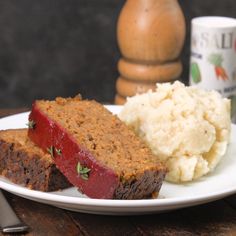 a plate with some meatloaf and mashed potatoes on it next to a mug