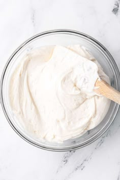 a glass bowl filled with whipped cream on top of a white marble countertop next to a wooden spoon