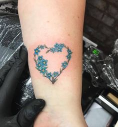 a heart shaped tattoo with blue flowers on the arm