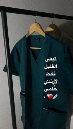 a green shirt with arabic writing on it hanging from a clothes rack next to a wall