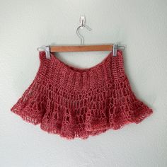 a red crocheted skirt hanging on a wooden hanger next to a white wall