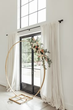 a white and gold wedding arch with flowers on it in front of a large window