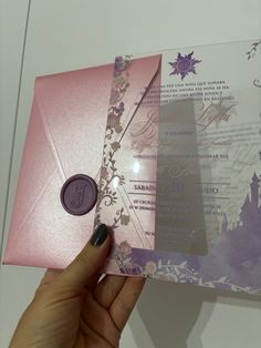 a person holding up a pink and purple wedding card with a wax stamp on it