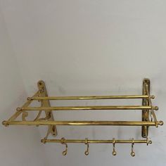 a gold metal rack with four hooks on it's sides and two hanging bars attached to the wall