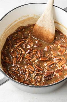 a wooden spoon in a pot filled with pecans and gravy on top of a white table