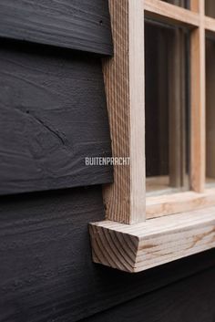 the side of a black house with wood trimmings and window panes on it