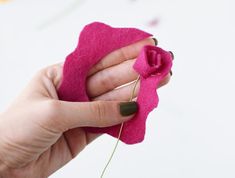 a hand holding a pink felt flower with green stems