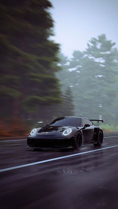 a black sports car driving down the road in front of some trees on a foggy day