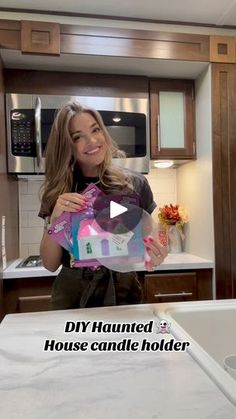 a woman is holding up a house shaped candle holder in her kitchen with the text diy haunted house candle holder