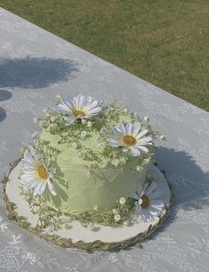 a green cake with daisies on it sitting on top of a white table cloth