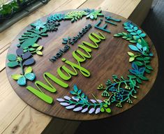 a wooden sign that says welcome with green and blue leaves on it, sitting on top of a table