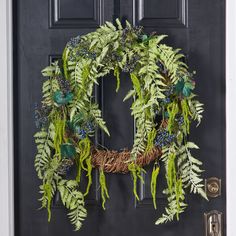 a wreath with green and blue flowers hanging from the front door, on a black door