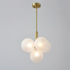 three white glass balls hanging from a brass chandelier against a gray background,