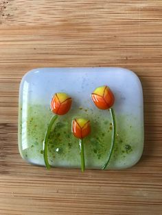 three orange and yellow tulips are on a white plate with green liquid in the middle