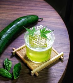 a cucumber sitting on top of a wooden table next to a glass filled with liquid