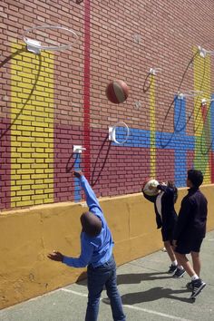 two boys are playing basketball in front of a brick wall with colorful artwork on it