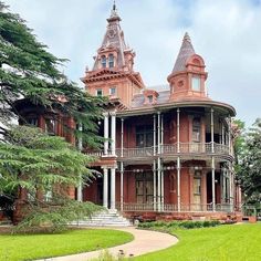 an old victorian style house in the middle of a grassy area with trees and bushes