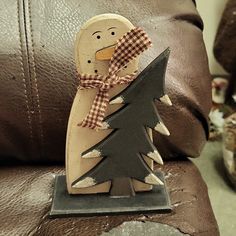 a wooden snowman holding a christmas tree on top of a brown leather chair in a living room