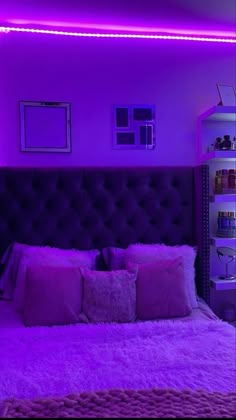 a bed with purple lighting in a bedroom next to a book shelf and pictures on the wall